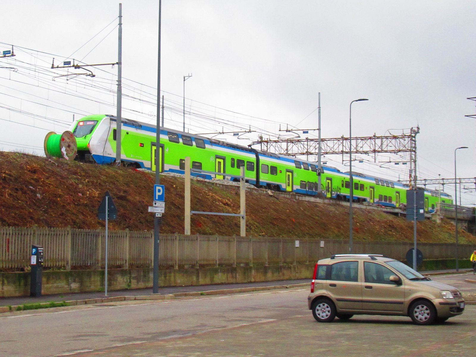Train Trenord Hitachi Caravaggio en déplacement, avec une vue de hauteur d'une voiture stationnée en bas, Milan Lombardie en Italie photo gratuite