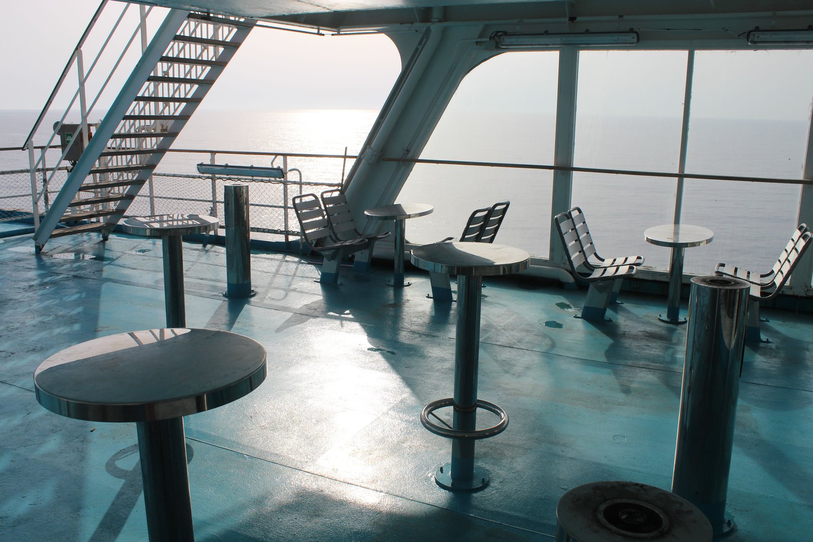 The exterior deck of a cruise ship, with tables, stools, and benches, offering a view of the sea, free photo