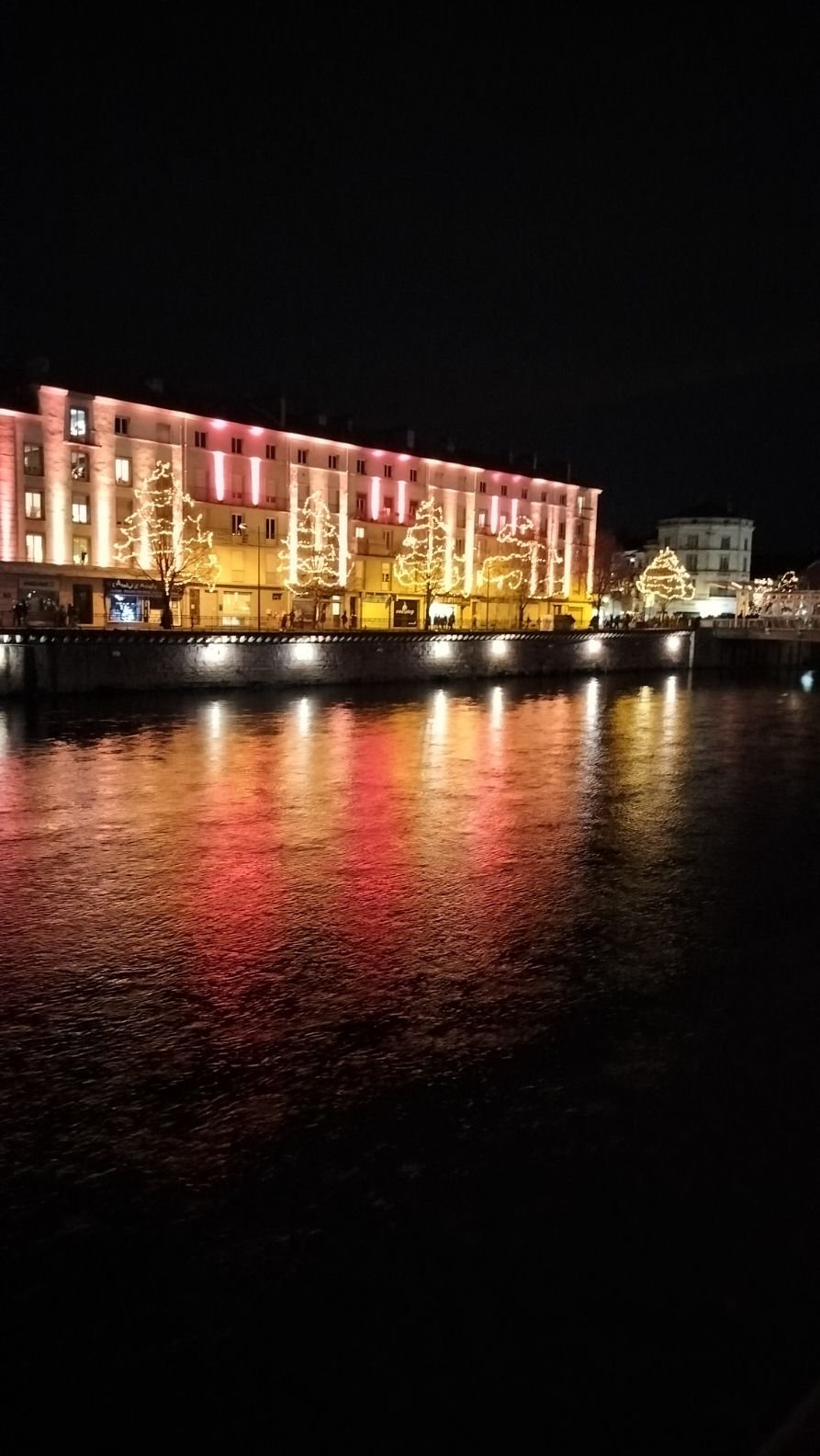 Bâtiment le long d'un cours d'eau la nuit, décoré d'illuminations festives, photo gratuite