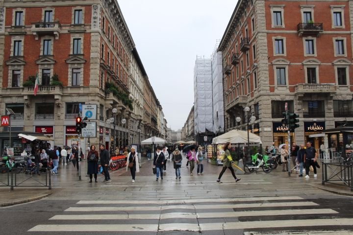 Rue piétonne, on y observe des bâtiments historiques, des passants, et des éléments urbains caractéristiques de la ville de Milan, photo gratuite