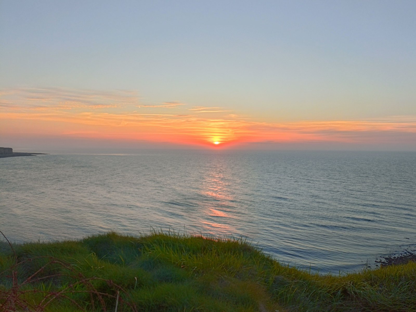 Un coucher de soleil sur l'océan, vu depuis une falaise herbeuse, photo gratuite