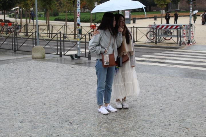Deux jeunes femmes se tenant sous un parapluie dans un espace public, photo gratuite
