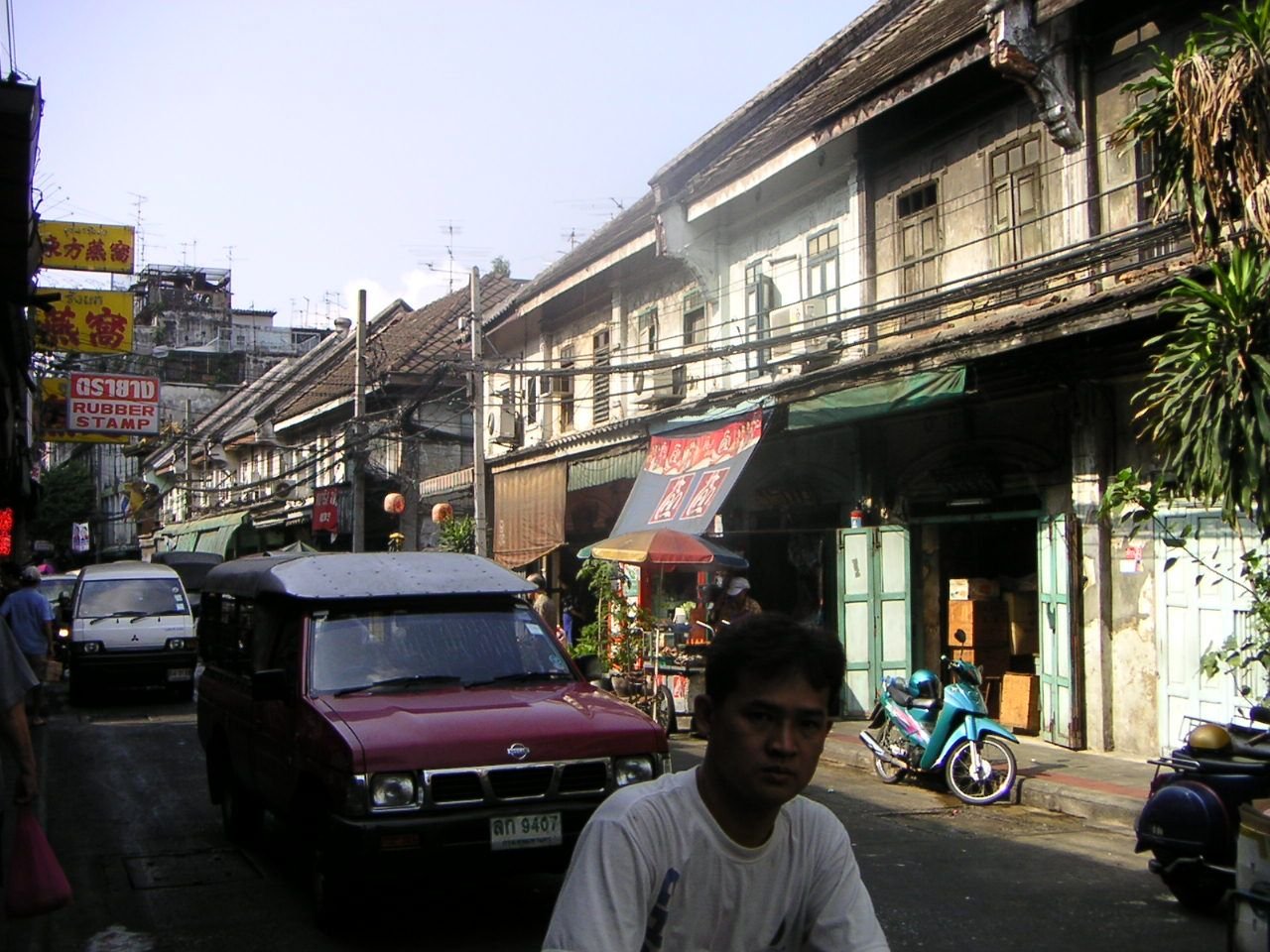 Une ruelle animée en Thaïlande, on y voit un homme, des voitures, des bâtiments, photo gratuite