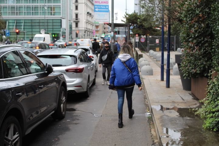 People walking on the edge of the tarmac, cars stopping at a red light, in the city of Milan Lombardy Italy free photo