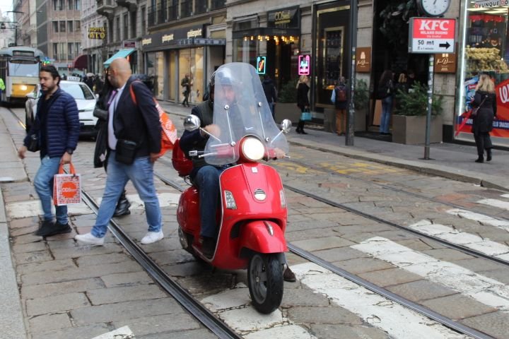 Un scooter rouge garé sur une voie pavée avec des rails de tramway dans la ville de Milan, photo gratuite