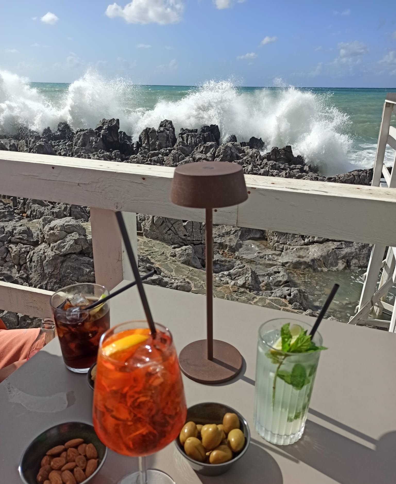 Un restaurant au bord de la mer, on voit une table avec plusieurs boissons (cocktails ou jus), des olives et des amandes sur une table, photo gratuite