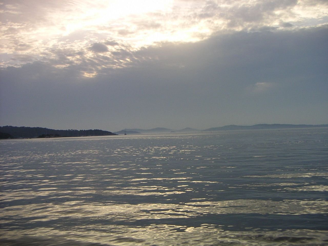 Une étendue d'eau calme avec des terres ou des îles lointaines à l'horizon, sous un ciel partiellement couvert de nuages, photo gratuite