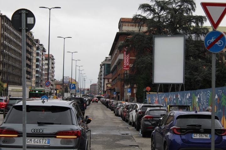 Voitures alignées en deux colonnes tout au long d'une rue créant un espace au milieu permettant le passage d'autres voitures, stoppées par un feu rouge dans la ville de Milan Lombardie en Italie photo gratuite