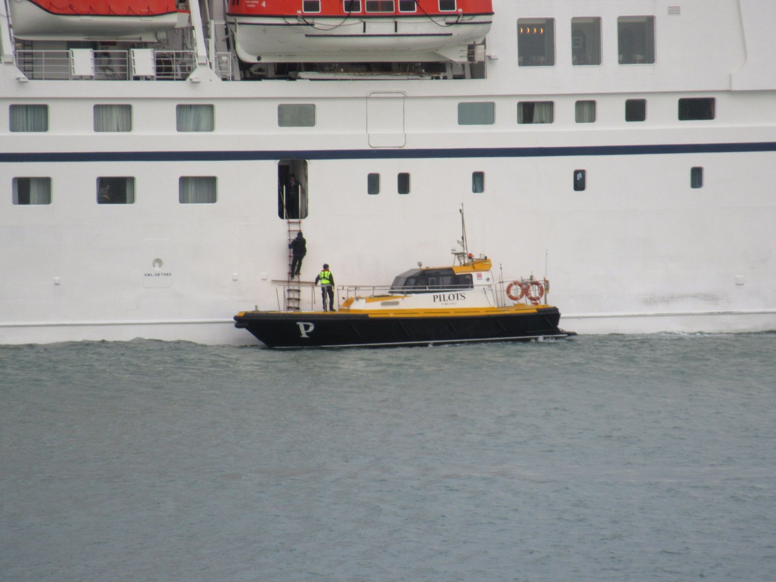 Bateau pilote collé a un bateau de croisière au bord de la mer, personne qui escalade l'échelle tentant d'atteindre l'intérieur du bateau photo gratuite