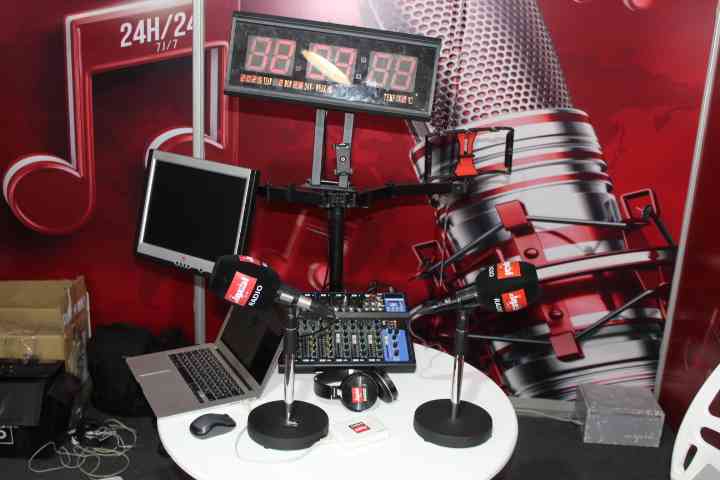 A radio or recording studio with two microphones, a laptop, an audio mixer, headphones, and a screen showing the time, free photo