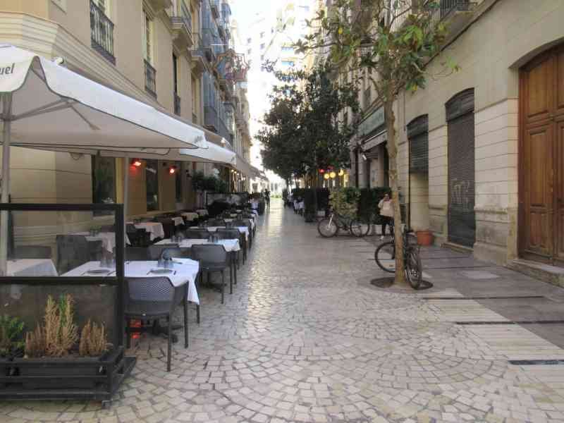 Ruelle pavée bordée d'immeubles, terrasse tables et chaises de restaurant installées sous des parasols à  Malaga, photo gratuite