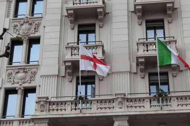 Des drapeaux, Lombardie et Italie, accrochés sur un balcon orné d'éléments architecturaux classiques sur la façade d'un bâtiment, photo gratuite