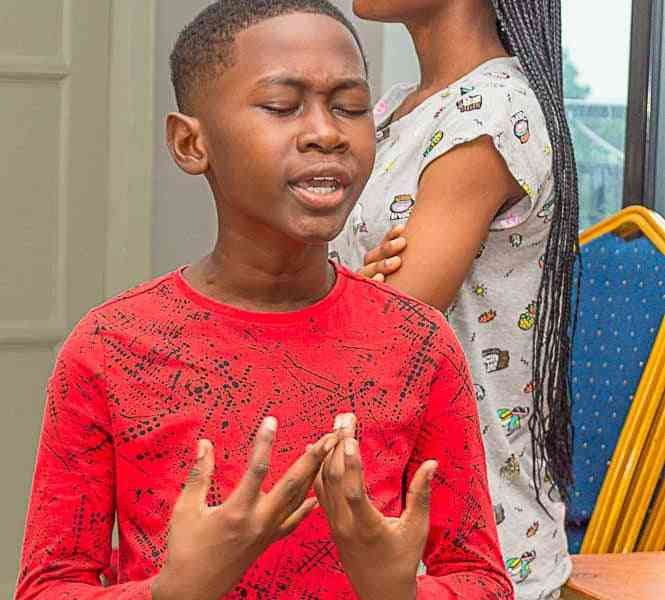 Un garçon en rouge, les yeux fermés et les mains levées photo gratuite