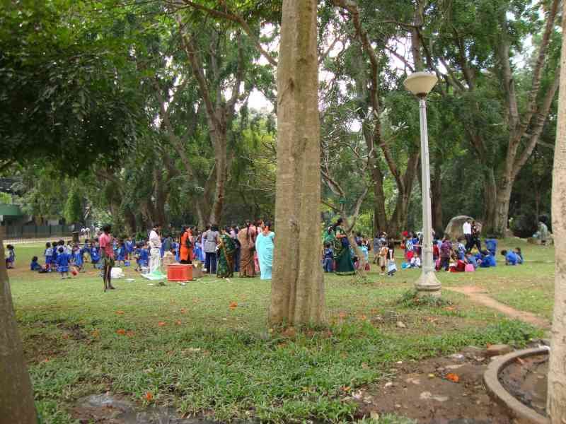 Un rassemblement de personnes, dont de nombreux enfants en uniforme scolaire bleu, dans un grand espace vert arboré, un jardin public, photo gratuite
