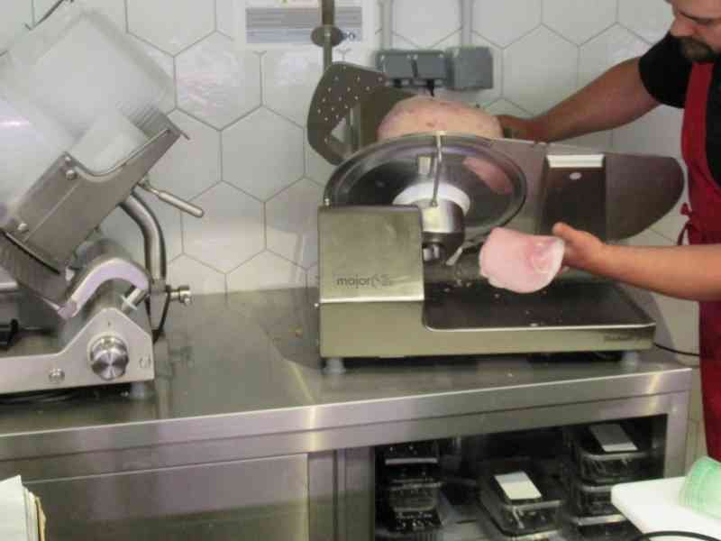 Homme découpant du jambon avec une trancheuse à jambon