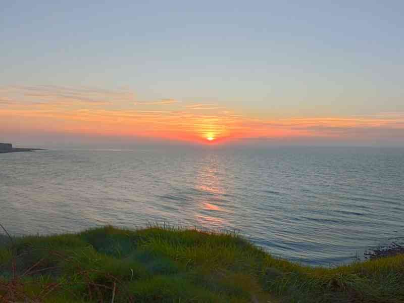 Un coucher de soleil sur l'océan, vu depuis une falaise herbeuse, photo gratuite