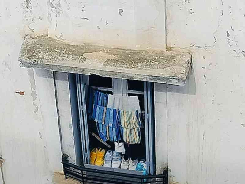 Paires de chaussures et vêtements suspendus pour sécher sur une fenêtre ouverte d’un bâtiment à façade blanche photo gratuite