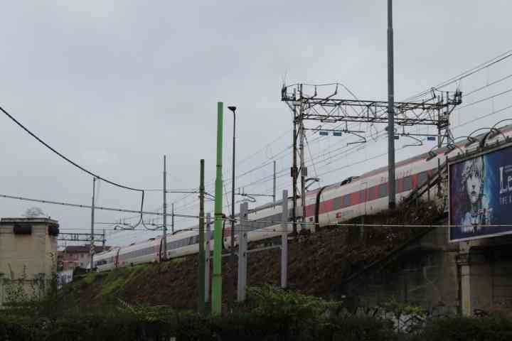 Un train sur une voie ferrée surélevée, des poteaux supportant des câbles électriques et des éléments de signalisation ferroviaire, photo gratuite