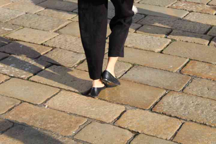 A person walking on a path paved with stone slabs wearing flat black shoes, free photo
