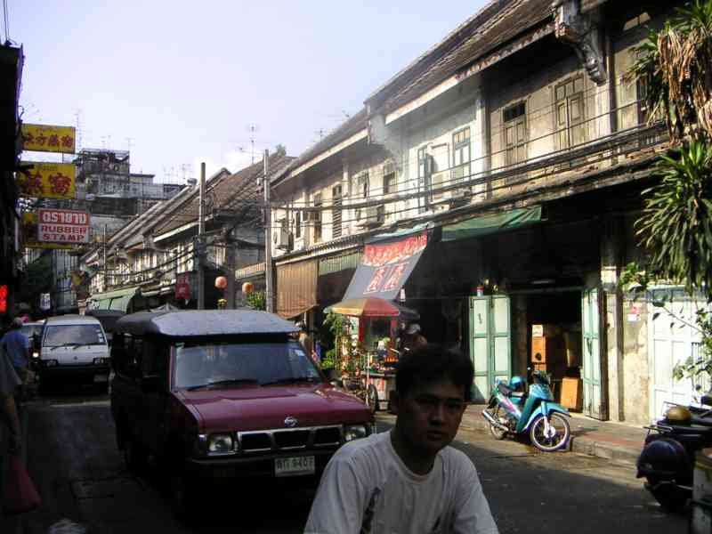 Une ruelle animée en Thaïlande, on y voit un homme, des voitures, des bâtiments, photo gratuite