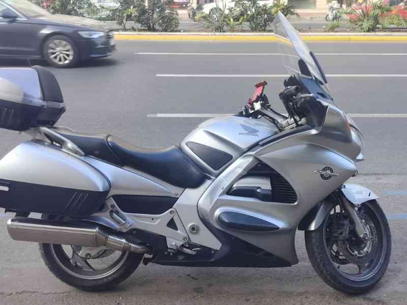 Une moto de marque Honda garée sur un trottoir - Uma moto da marca Honda estacionada num passeio, moto tipo touring na cor prata/cinza metalizado Foto gratuita