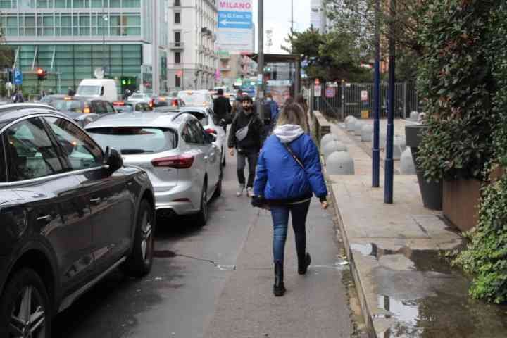 People walking on the edge of the tarmac, cars stopping at a red light, in the city of Milan Lombardy Italy free photo