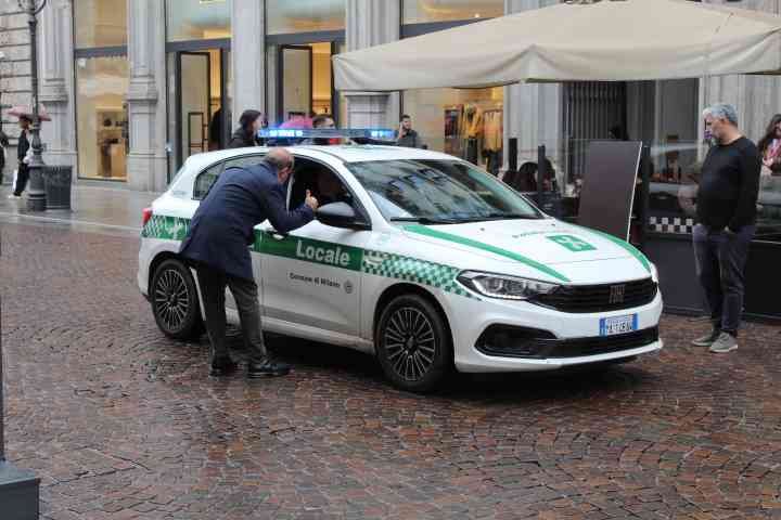 Une interaction entre un agent et une personne à côté d'une voiture de police de la Polizia Locale italienne, dans un environnement urbain, photo gratuite