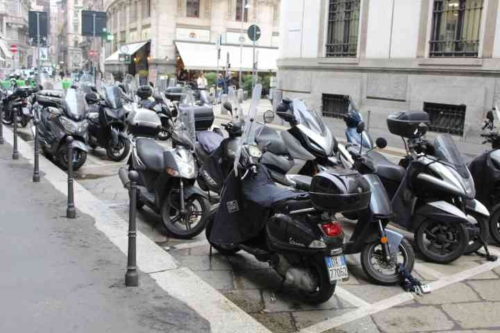 Un stationnement de scooters et de motos garés le long d'un trottoir dans une rue urbaine de Milan, photo gratuite