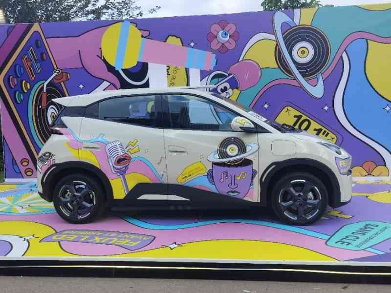 A BYD Seagull, a small electric city car, in front of a wall covered in graffiti, free photo