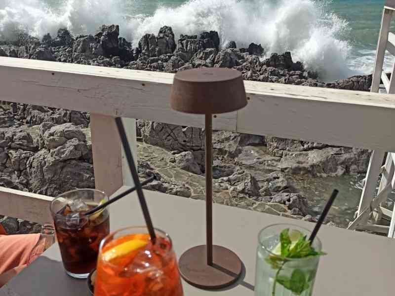 Un restaurant au bord de la mer, on voit une table avec plusieurs boissons (cocktails ou jus), des olives et des amandes sur une table, photo gratuite